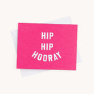 A vibrant, bright pink greeting card from Simplifieds Boxed Card Set reads HIP HIP HOORAY in white text. Perfect for any occasion, it rests on a white surface with a partially visible white envelope beneath.