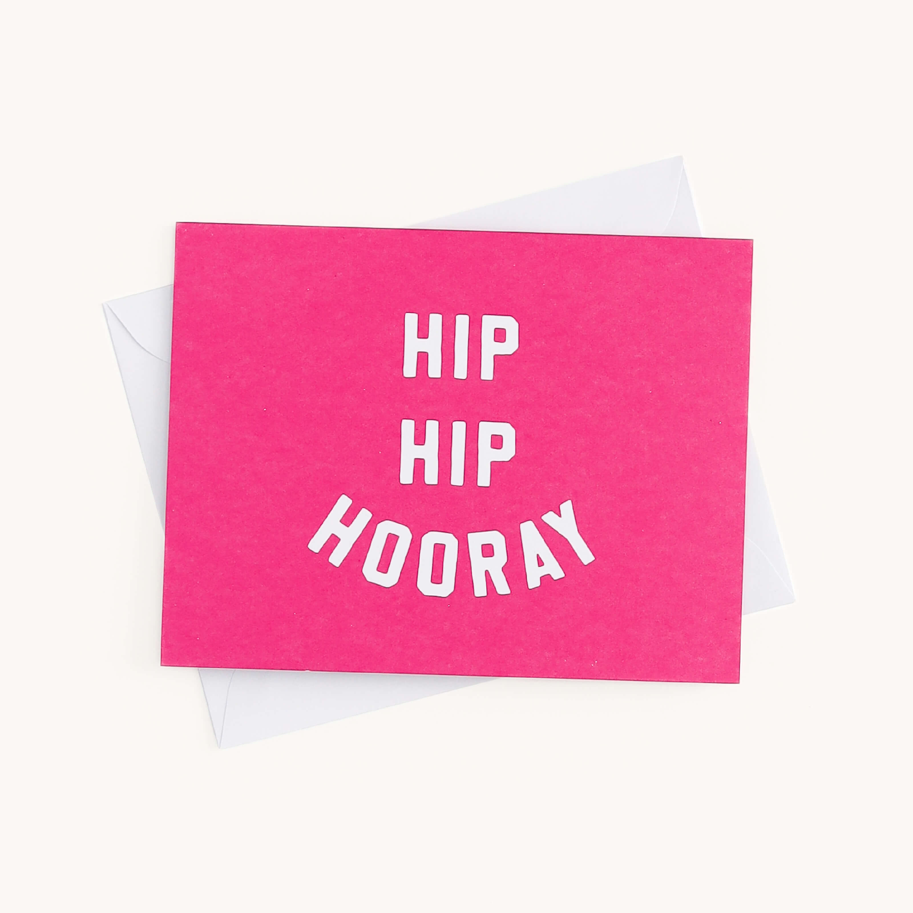 A vibrant, bright pink greeting card from Simplifieds Boxed Card Set reads HIP HIP HOORAY in white text. Perfect for any occasion, it rests on a white surface with a partially visible white envelope beneath.