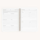 The Simplified Workbook - Meal Planning is an open spiral-bound planner featuring sections for Simplified Meals and a Perpetual Grocery List, with pages organized into categories like produce, frozen, and miscellaneous for efficient meal planning and grocery shopping.