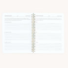 The Simplified Workbook - Wellness is a spiral-bound notebook featuring lined pages. The left page includes sections for My Morning Routine, My Evening Routine, and My Weekly Routine to track goals, while the right page offers sections for small tasks or self-care activities, leaving space for creativity.