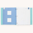 The Baby Book - Mint by Simplified features a customizable blue left page with star patterns and Babys Debut frames, while the white right page provides writing space with a bookmark icon for personal notes. Add personalized moments with customizable page packs.