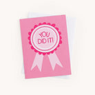 Celebrate the occasion with a pink greeting card from the Simplified Boxed Card Set. Featuring YOU DID IT! in a ribbon design, the darker pink ribbon with light pink tails sits atop a white envelope, perfect for conveying heartfelt congratulations.