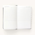 The 2024-2025 Daily Dapperdesk Planner - Black Tie by Simplified features a luxurious leatherette cover, with each double-page spread displaying daily schedules. For example, the left page shows Tuesday, August 6, 2024, and the right page shows Wednesday, August 7, 2024. Time slots from 7 a.m. to 8 p.m. offer lined spaces for notes alongside handy tabs.