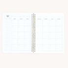 The Workbook - Wellness by Simplified is a spiral-bound, minimalist planner with a clean white backdrop. It offers a one-month calendar from Monday to Sunday, featuring blank squares and a notes section, perfect for tracking self-care goals.