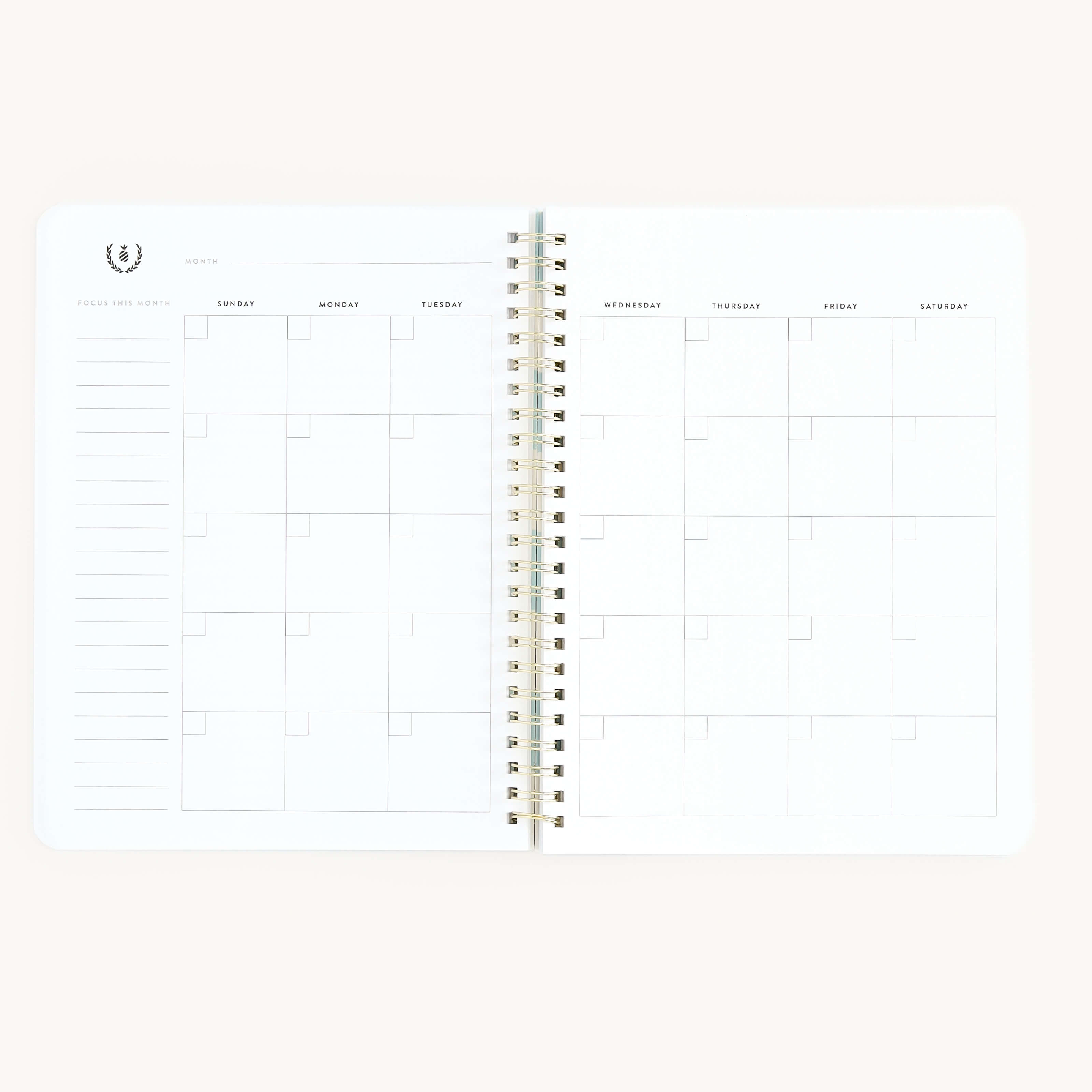 The Workbook - Wellness by Simplified is a spiral-bound, minimalist planner with a clean white backdrop. It offers a one-month calendar from Monday to Sunday, featuring blank squares and a notes section, perfect for tracking self-care goals.