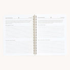 The Workbook - Finances by Simplified is an open spiral-bound notebook with lined pages, featuring sections like LOOKING BACK and LOOKING AHEAD, with prompts such as WHAT WORKED LAST YEAR, WHAT DIDNT WORK, and GOALS FOR NEW YEAR. Its ideal for managing money and tracking financial goals.