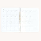 The Workbook - Wellness by Simplified is an open spiral-bound planner on a light background, with a weekly layout for goal tracking. Each day is labeled at the top with spaces for notes or tasks, and the lower section includes areas for checklists or self-care entries.