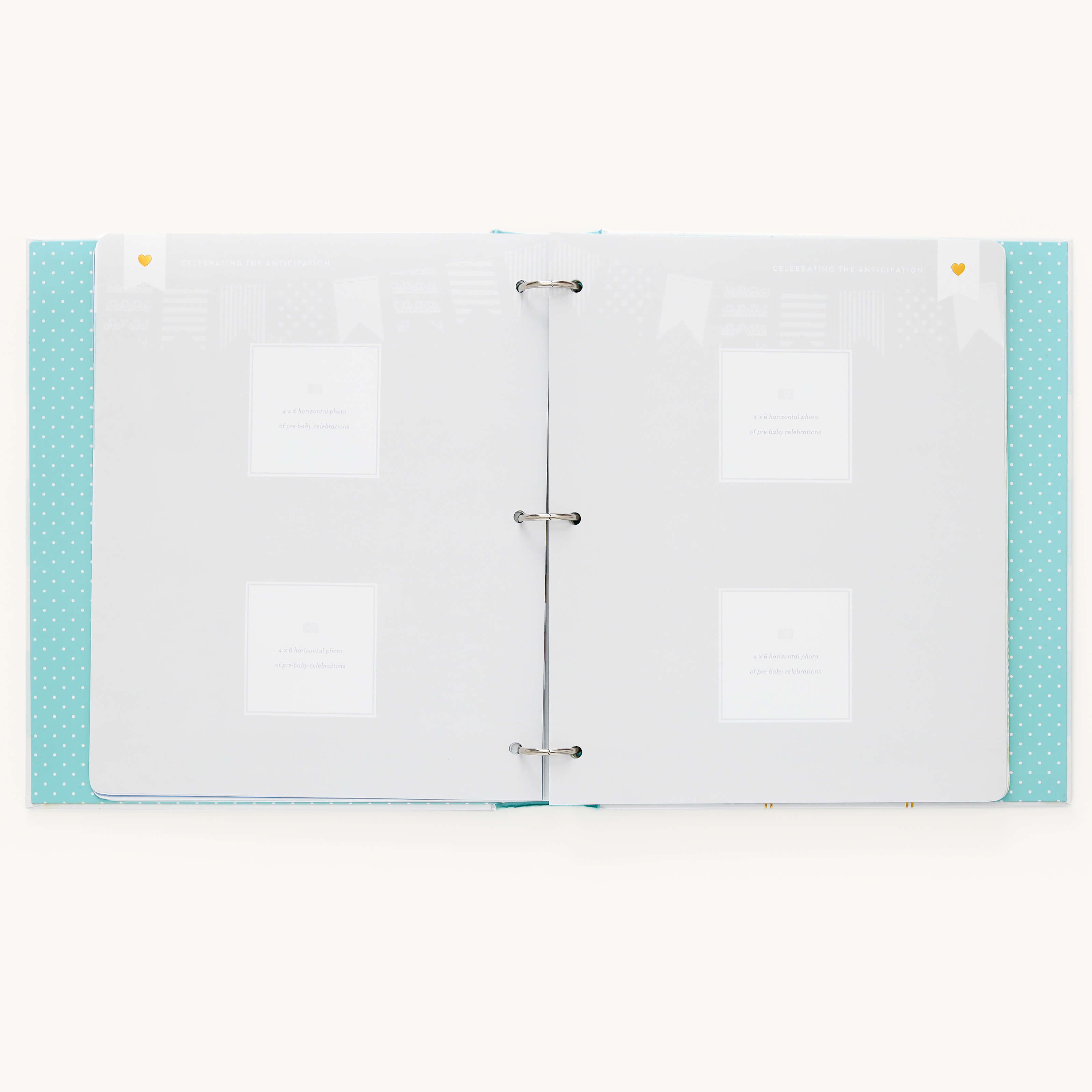 The Baby Book - Mint by Simplified is an open, light blue polka-dotted binder with blank white pages. It includes guided writing spaces, four photo placeholders, and faint decorative patterns featuring tiny heart icons in the corners.