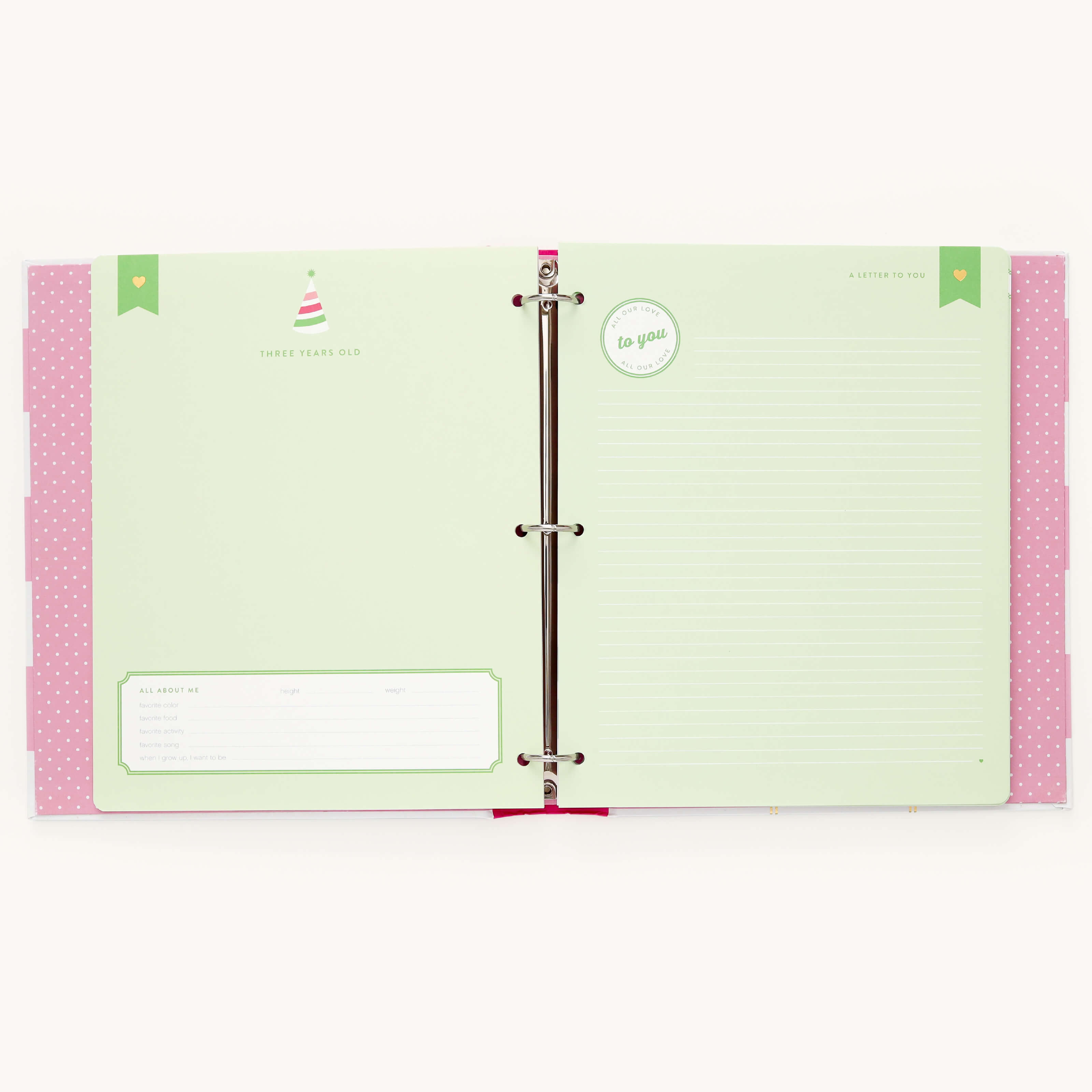 The Simplified Big Kid Book - Raspberry features colorful pages with a pastel green spread, including A Letter to You on the right and an All About Me form on the left. The playful pink polka dot cover edges and birthday hat graphic add charm.