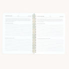 A Simplified Workbook - Wellness lies open on a white surface, containing sections called Simplified Wellness, Looking Back, and Looking Ahead. It includes prompts such as What worked last year? and Ideas for new routines to assist in goal tracking and self-care enhancement.