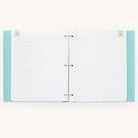 An open Simplified Baby Book - Mint binder with a light blue cover and polka dot pattern is shown. Inside, customizable page packs offer guided writing space with faint lines and decorative banners. Its perfect for crafting a personalized baby book on any flat surface.