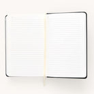 The 2024-2025 Daily Dapperdesk Planner - Black Tie by Simplified is open, showcasing lined pages and a cream ribbon bookmark against a white background. This sleek planner boasts a black leatherette cover, perfect for organizing your plans over the next 12 months.