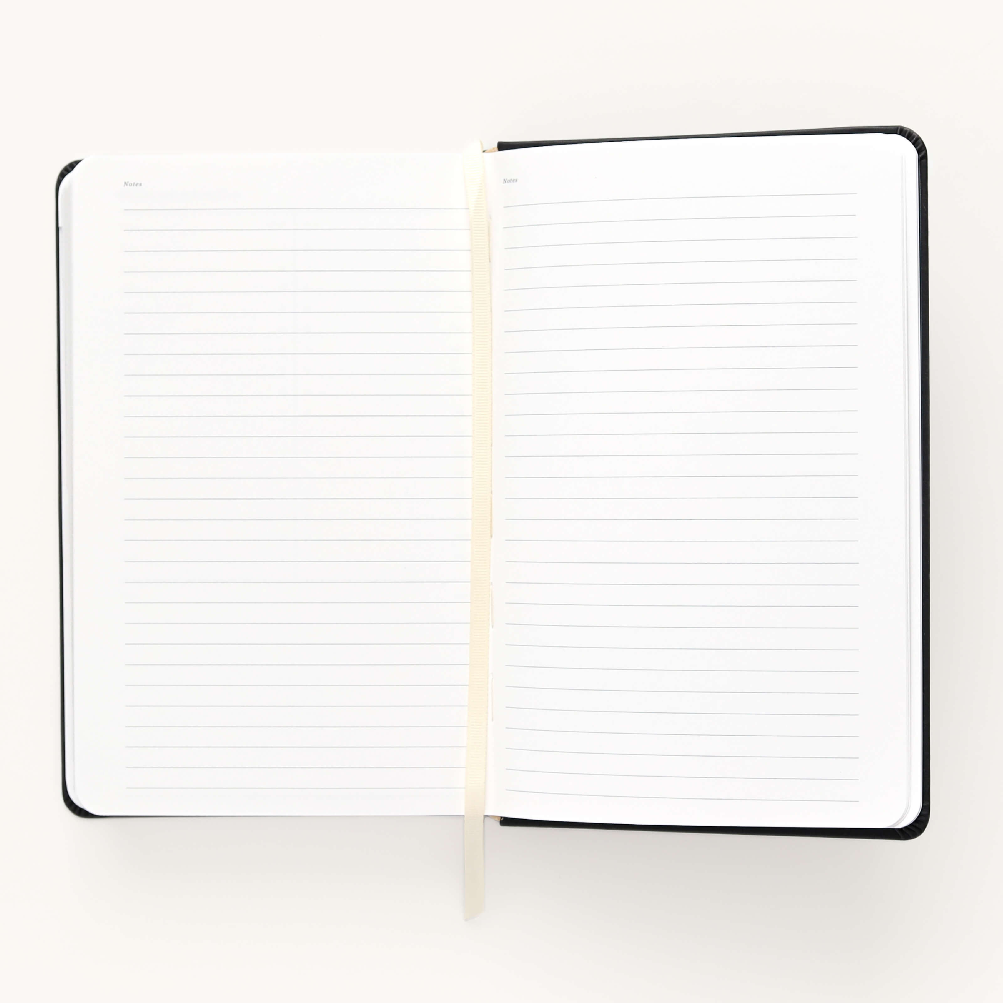 The 2024-2025 Daily Dapperdesk Planner - Black Tie by Simplified is open, showcasing lined pages and a cream ribbon bookmark against a white background. This sleek planner boasts a black leatherette cover, perfect for organizing your plans over the next 12 months.