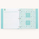 The open Baby Book - Mint by Simplified shows a customizable page pack with small sailboats. The left page is titled Announcing Your Arrival with fields for details. The right page has guided writing space and two square photo placeholders bordered by small dots.