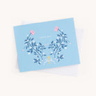 A Simplified Boxed Card Set includes a blue thank you card with elegant floral designs of pink and yellow flowers, green leaves on the front, and an envelope partly visible behind it, perfect for any occasion.