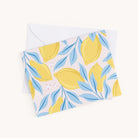 Simplifieds Boxed Card Set includes a versatile greeting card with a charming lemon and leaf pattern in yellow and blue on light pink. Perfect for any occasion, it comes partially tucked in a white envelope—an ideal addition to your collection for all your greeting needs.