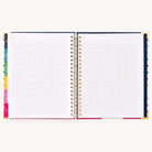 The Undated Teacher Planner - Happy Stripe by Simplified features colorful tabbed dividers, spiral binding, and graph paper pages perfect for lesson planning and tracking student progress. The mostly blank pages invite creativity, all set against a light background.