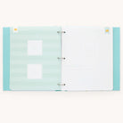 The Baby Book - Mint by Simplified features a two-ring binding with a guided writing space. The left page is light blue with white stripes and two labeled photo slots; the right has your nursery and lines for notes. The polka-dotted cover is blue, and it offers customizable page packs.