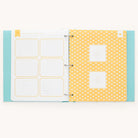 The Baby Book - Mint by Simplified offers a guided writing space with a blue polka dot cover. The left page is sectioned for notes with a yellow border, while the right page features a yellow background with white clouds and two empty photo frames, perfect for personalizing your baby book.