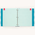 The Big Kid Book - Teal by Simplified is open, showing striped pages with polka dot edges and two red bookmarks in the top corners. Its metal rings at the center make it a perfect binder for tracking child growth milestones.