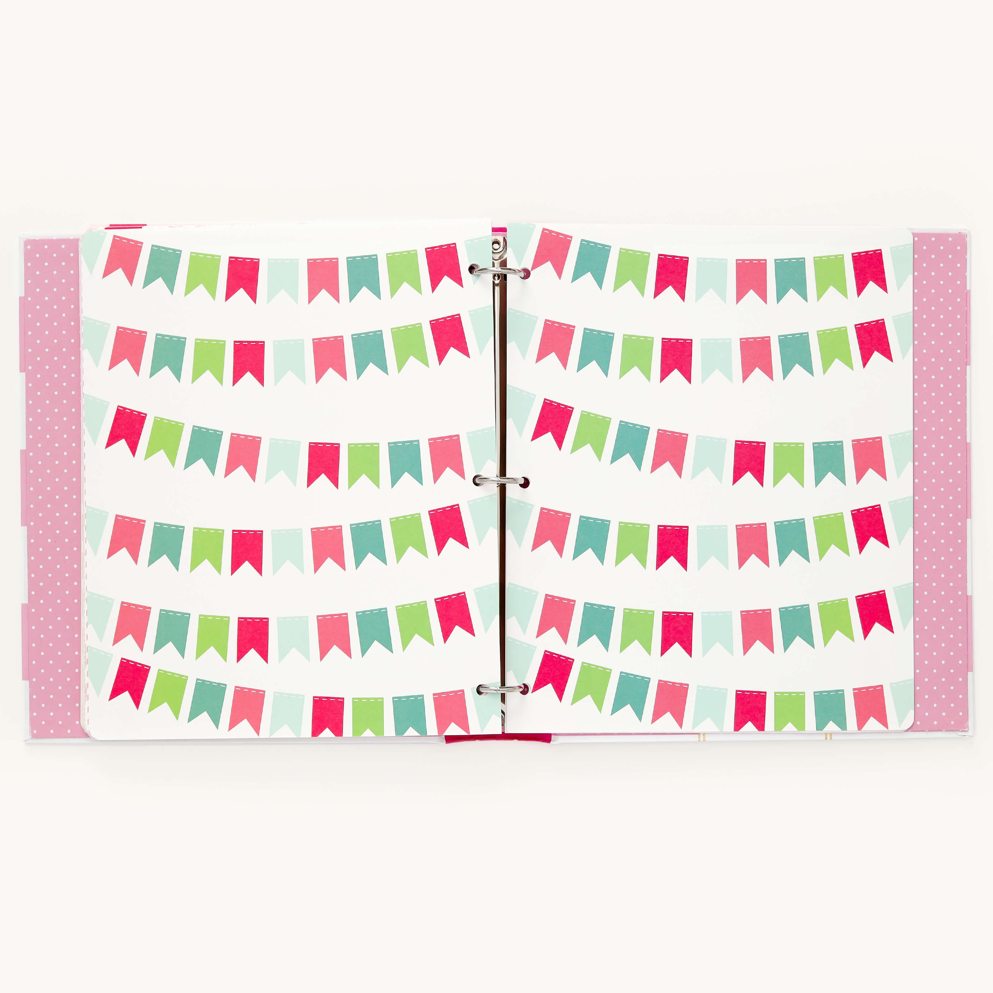 An open scrapbook showcases colorful pages with vibrant bunting banners in red, green, and blue, bound by metal rings. Reminiscent of Simplifieds Big Kid Book - Raspberry, the cover sports a playful pink polka dot pattern.