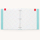 The Baby Book - Mint by Simplified is an open scrapbook with white pages adorned with colorful polka dots and red ribbon bookmarks. The cover edges have a light blue polka dot design. This customizable baby book includes guided writing spaces, ideal for capturing precious memories.