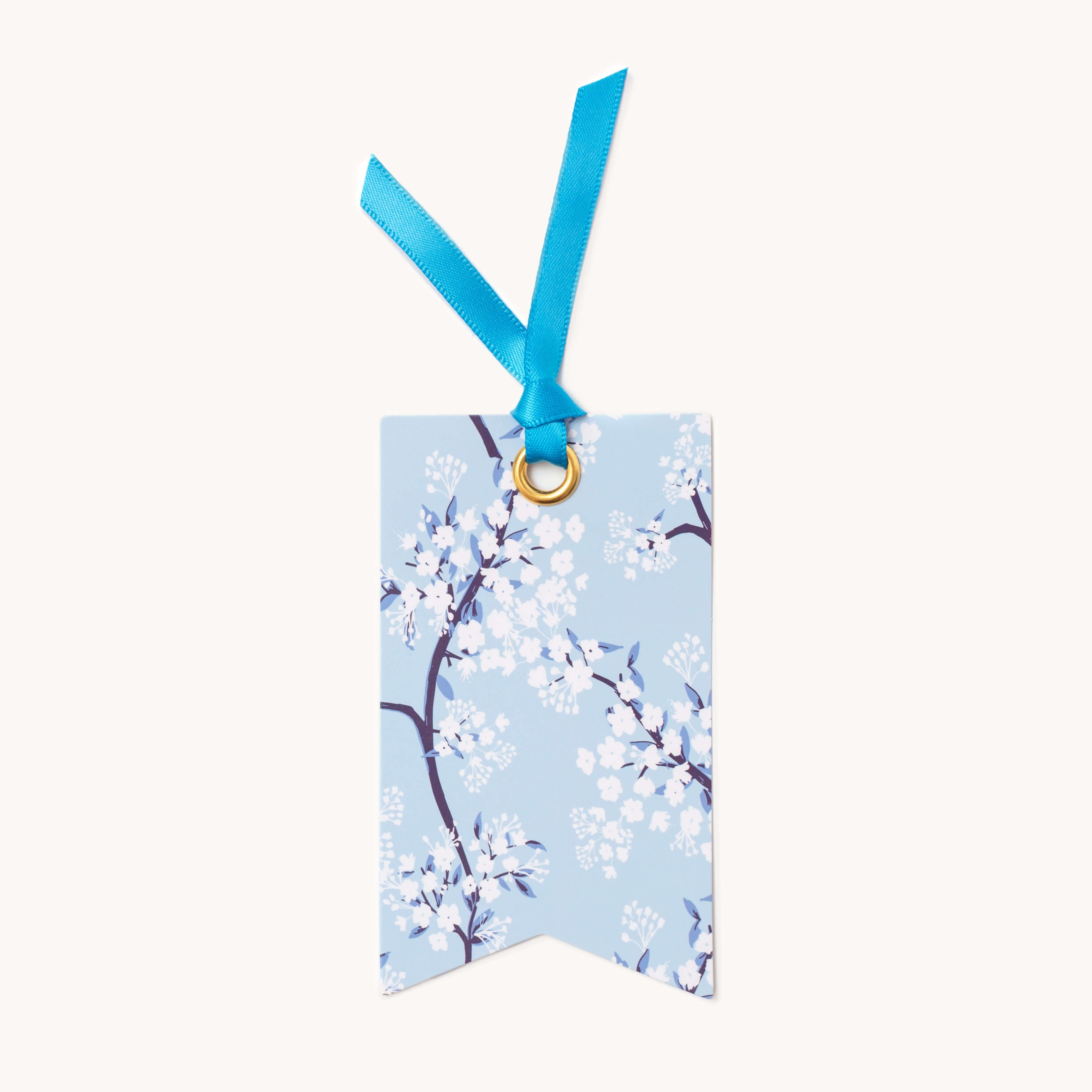 The Gift Tag Set - Cherry Blossoms by Simplified features rectangular tags with a light blue background showcasing delicate white and blue floral patterns. A blue ribbon threads through a gold grommet to add an elegant touch—perfect for enhancing your gifts.